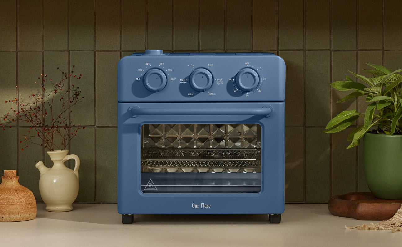 Blue toaster oven on a kitchen counter with decorative items in the background