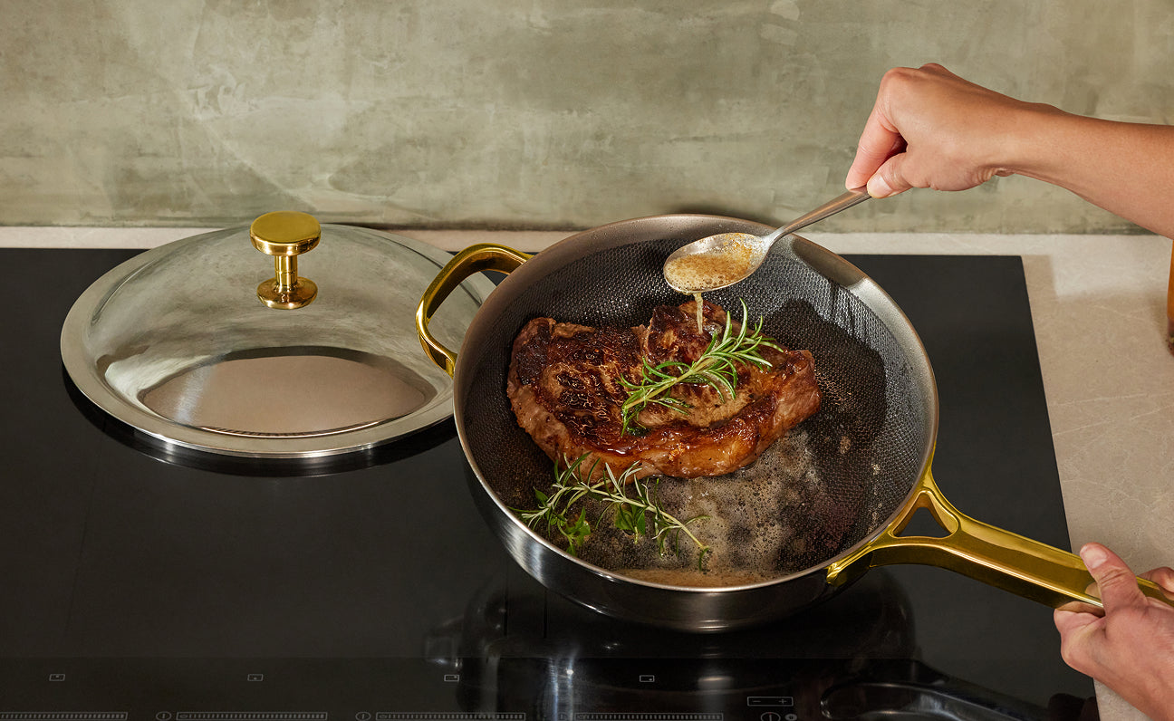 Person cooking pork chops with herbs in a frying pan on a stove.