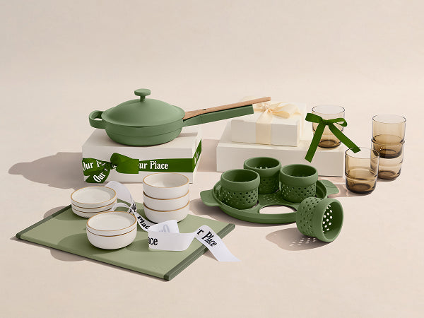 Green kitchenware set including pots, bowls, and a cutting board on a beige background.