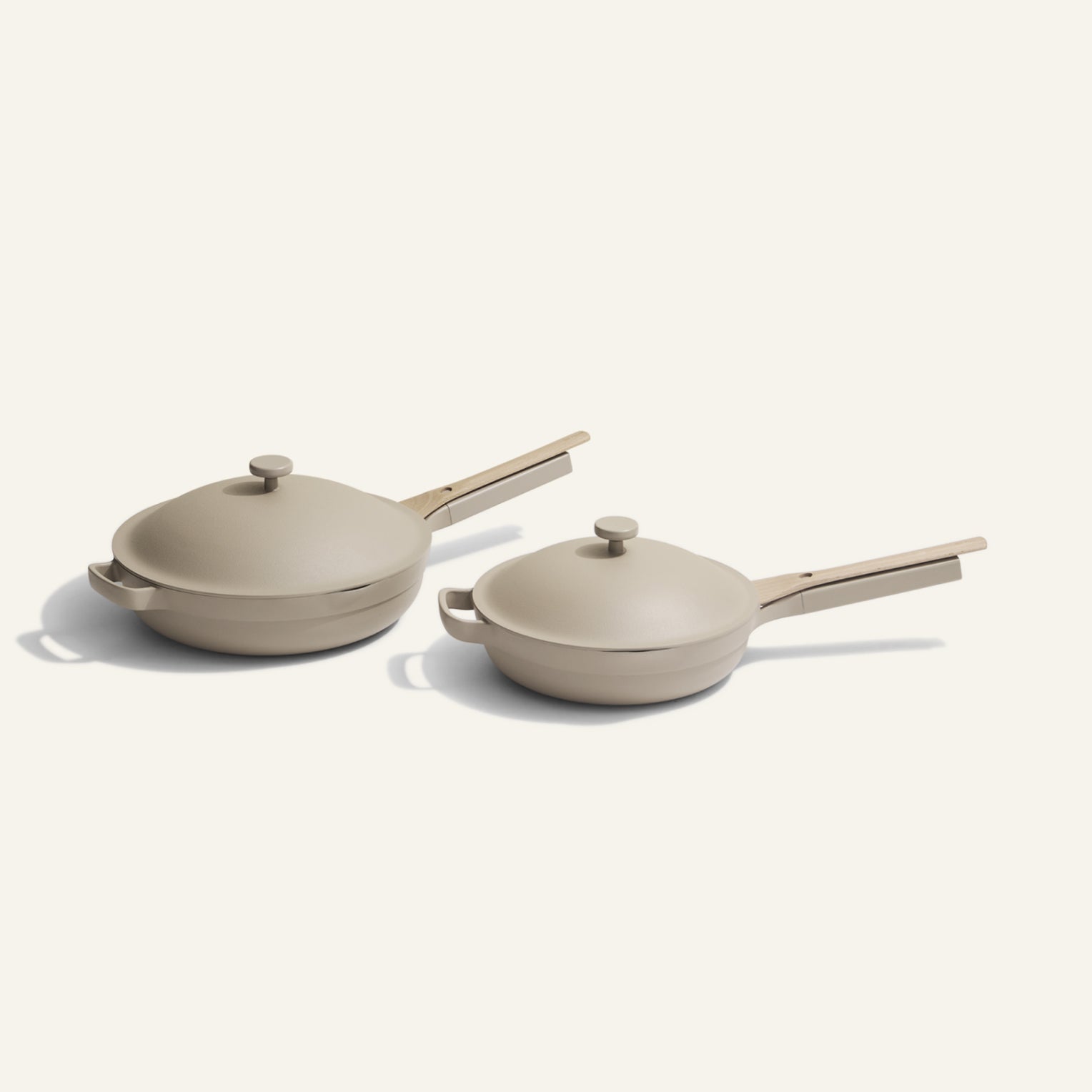 The Always Pan Duo features two beige ceramic sauté pans with matching lids and handles in different sizes, placed side by side on a light background—highlighting their versatile cookware style.