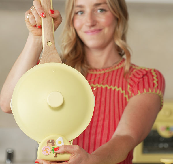 Woman holding a yellow pan with a wooden spoon